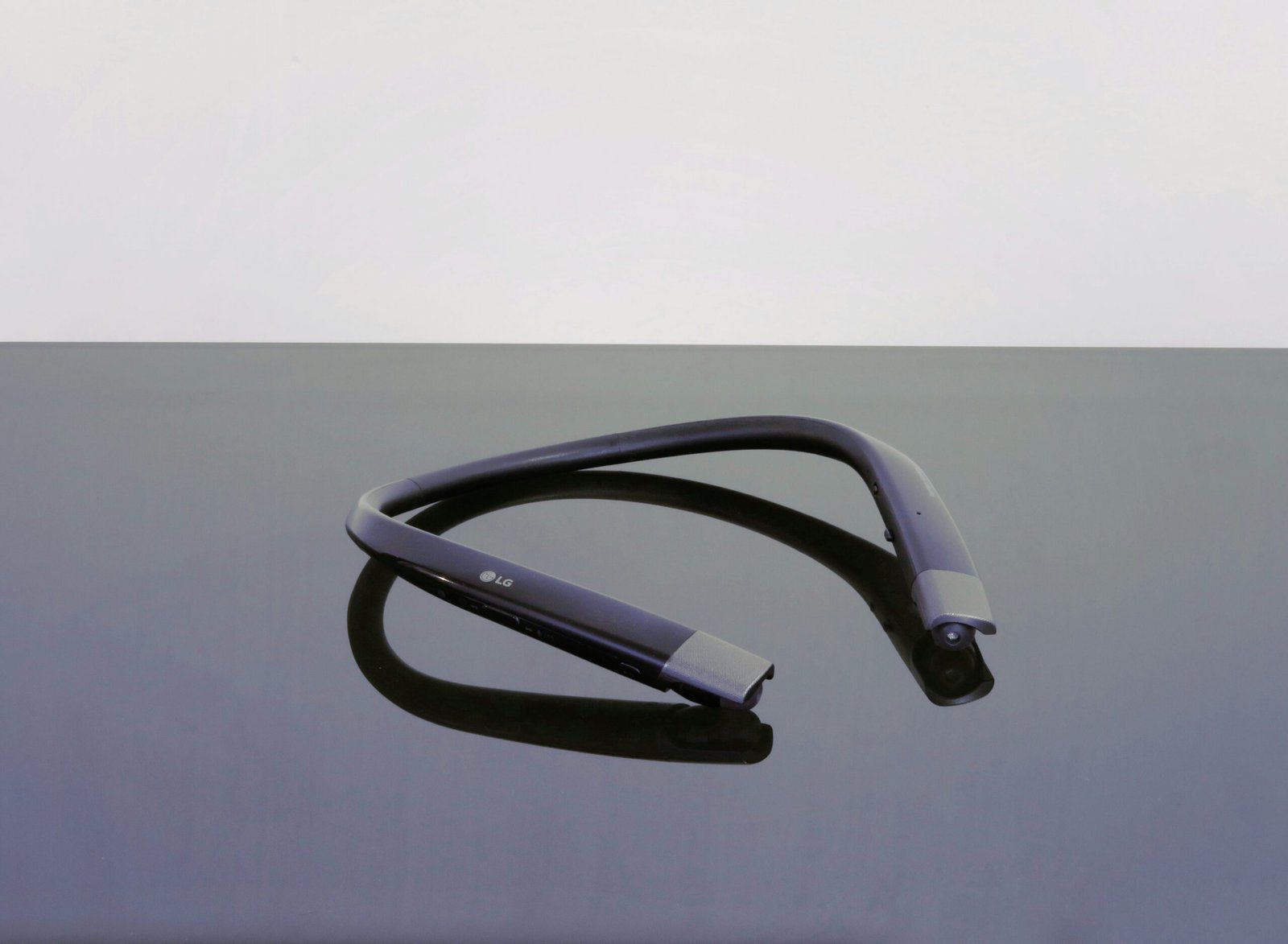 Photo of a dark gray neckband headphone on a darker background.