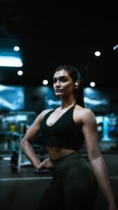 A girl in gym clothes posing inside a gym with ear phones on. The image is from Unsplash and belongs to Daniel-Azamanov