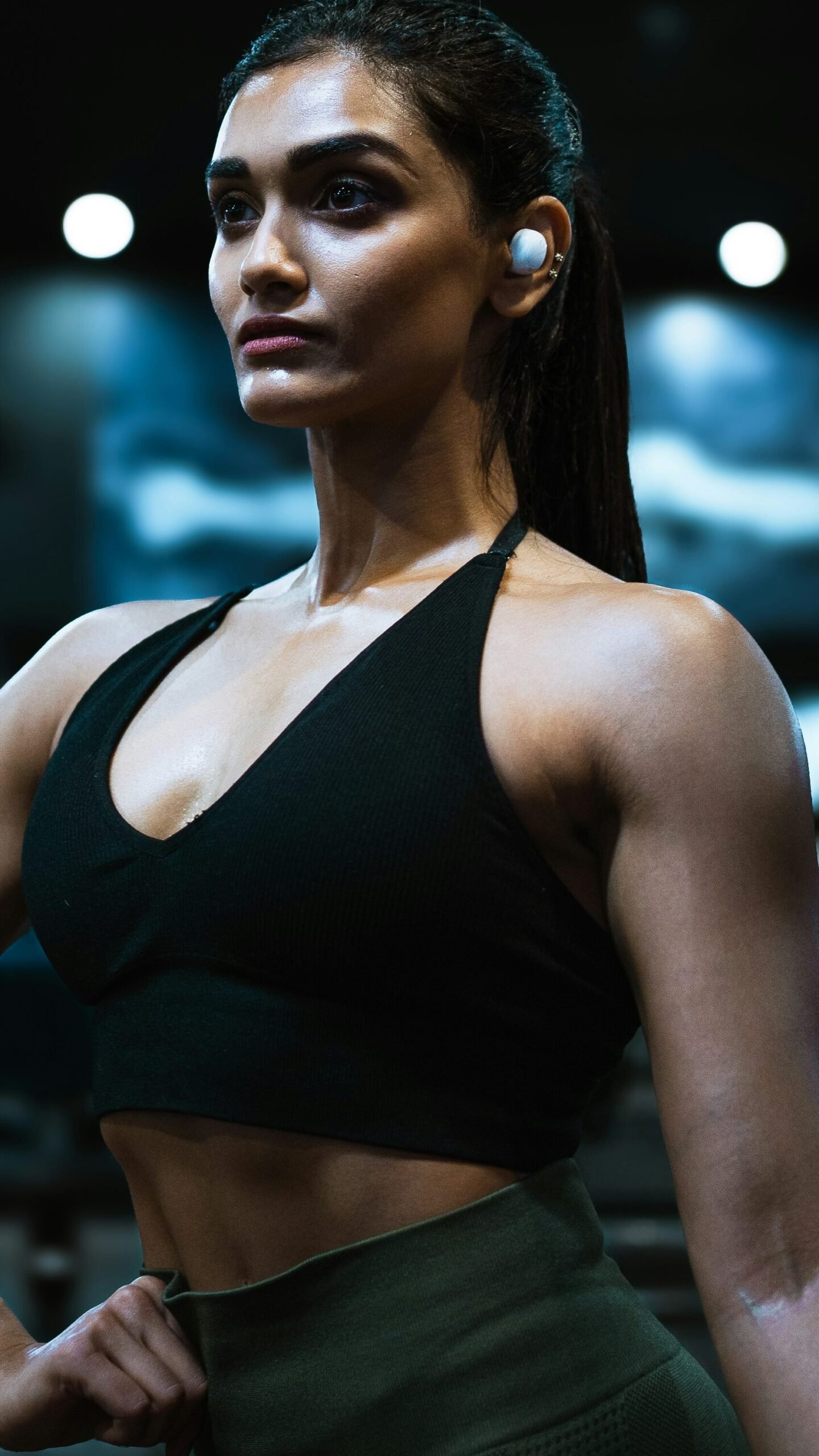 A girl in gym clothes posing inside a gym with ear phones on. The image is from Unsplash and belongs to Daniel-Azamanov