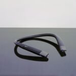 Photo of a dark gray neckband headphone on a darker background.